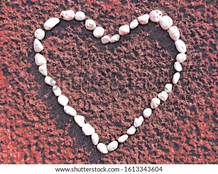 Heart made of small white pebbles on sand in red closeup