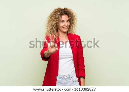 Young blonde woman with curly hair over isolated green background happy and counting three with fingers