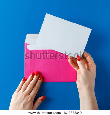 Pink envelope with a greeting card in the hands of a young woman.