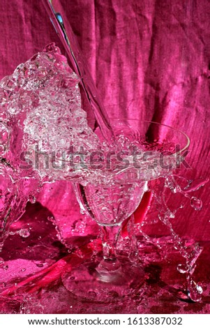 A splash of water in a clear glass goblet with a pink backdrop