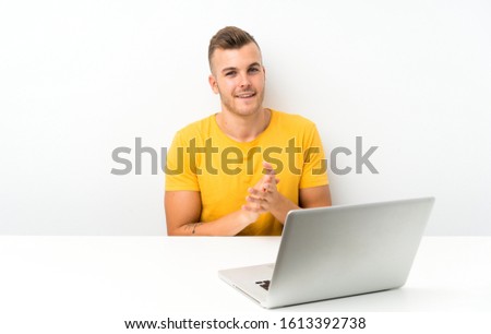Young blonde man in a table with a laptop applauding