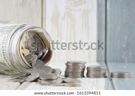 Saving concept. Coins and notes in a jar and on a wooden surface