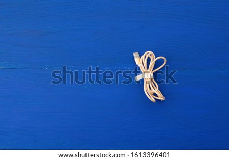 twisted golden cable for charging with electricity equipment in textile winding on a blue wooden background, close up