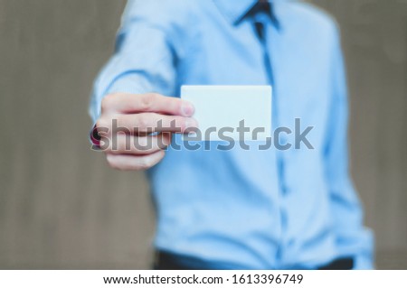 Young business man holding white business card on modern office blur background.