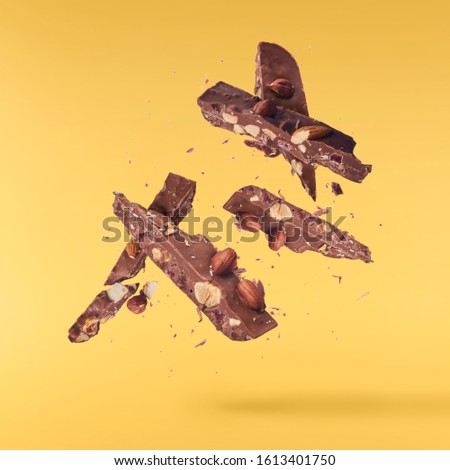 Pieces of chocolate with nuts flying in the air isolated on yellow background. High resolution image. Food levitation concept.
