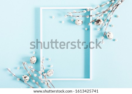 Easter holiday composition. Blank frame for text, easter eggs and willow branch on pastel blue background. Flat lay, top view, copy space