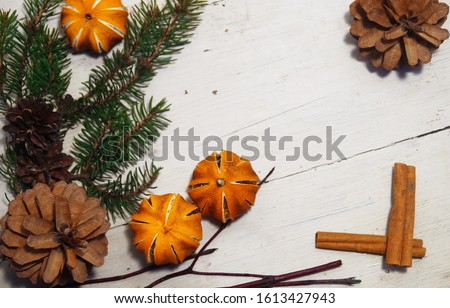 Photo of a Christmas background with a fir branch, a shelf of cinnamon, dried mandrins and cedar cones on an old wooden table with cracked paint.