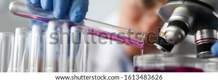 Female chemist holds test tube of glass in hand closeup overflows liquid solution potassium permanganate. Conducts an analysis reaction takes various versions reagents using chemical manufacturing Royalty-Free Stock Photo #1613483626