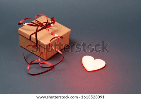 Gift box with red ribbon and a wooden heart on a gray background. Red backlight