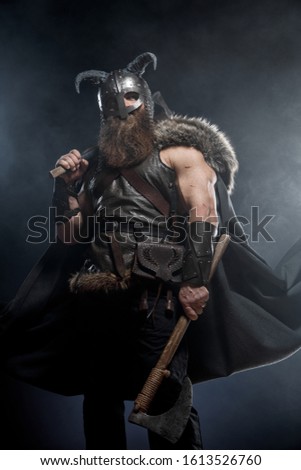 Medieval warrior berserk Viking with axes attacks enemy. Concept historical photo of Scandinavian god in armour and helmet with horns