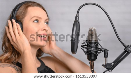 Girl sings into a microphone, in headphones in a studio. Producing and creating songs, music, recording a track. Writing an album