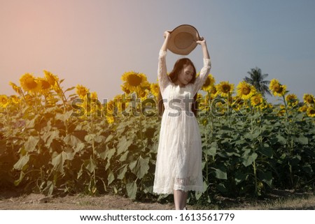 The image of a lovely Asian woman is fun and happy in a variety of gestures and tossing a hat in a sunflower-growing field. 