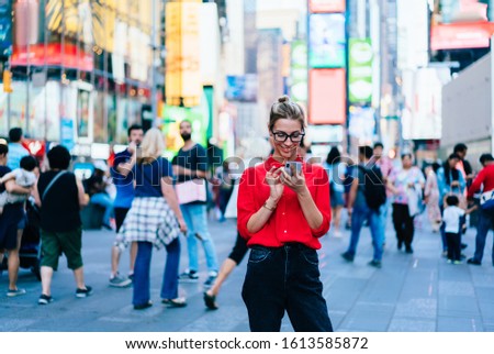Caucasian female standing in crowded square with mobile phone in hands.Addicted to social network. Millennial technology user. Young woman browsing internet via app on smartphone. Tourist explore city