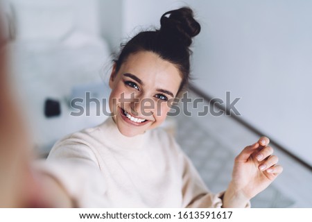Pretty young female with big smile standing at bedroom after work with laptop and having fun taking light cheerful selfie on blurred background Royalty-Free Stock Photo #1613591617
