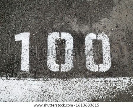 Number 100 on the asphalt surface. Marking line. Close-up.