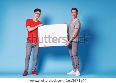 Advertising. Your text here. Couple of handsome young men holding an empty board with copy space together on blue background.