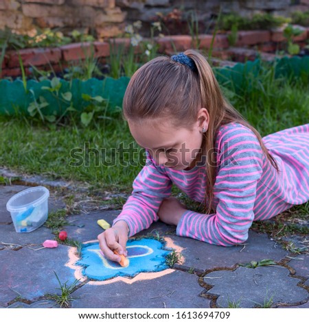 top view of a schoolgirl who draws on the sidewalk in a summer garden