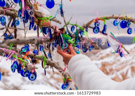 woman hand holding Blue evil eye / nazar boncugu, Turkish symbols hanging on a tree; Cappadocia