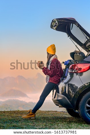 Woman traveller enjoy coffee time on back storage of car with scenery view of the mountain and mist morning in background Royalty-Free Stock Photo #1613737981
