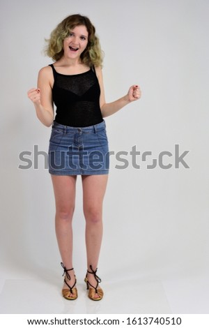 Full-length portrait of a pretty girl with beautiful curly hair. A horizontal photo concept of a young woman in a black t-shirt and blue skirt is standing in front of the camera on a white background.