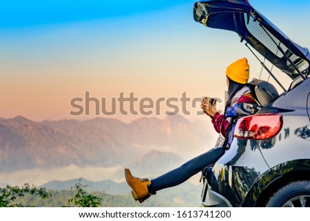 Woman traveller enjoy coffee time on back storage of car with scenery view of the mountain and mist morning in background