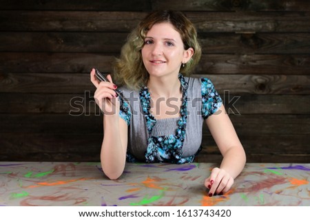 Horizontal photo concept of a cute young woman in a turquoise sweater. Portrait of a pretty girl with beautiful curly hair sitting at a decorated table on a wooden background.