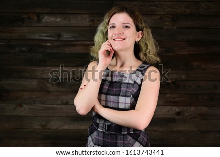 A horizontal photo concept of a cute young woman with emotions in a checkered dress. Portrait of a pretty girl with beautiful curly hair stands in front of the camera on a wooden background.