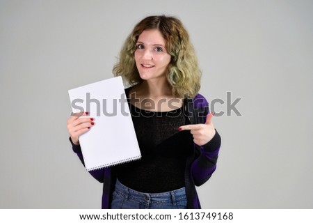 Concept horizontal photo of a young woman with emotions in a dark jacket standing in front of the camera on a white background. Portrait of a student girl with a folder in her hands with fluffy hair.