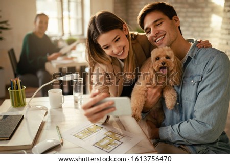 Happy business couple and their poodle having fun while taking selfie in the office. 