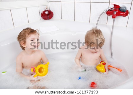 Two little boys having fun with water by taking bath in bathtub
