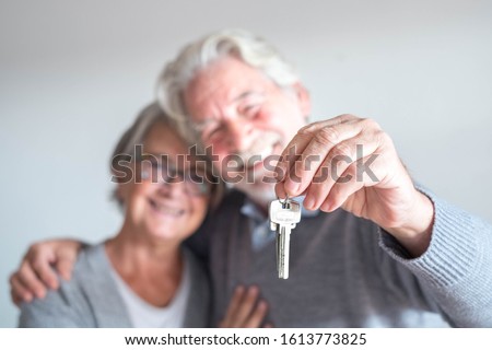 couple of two seniors after buy a new house or car and go to live together - man holding a key and mature man and woman looking at it Royalty-Free Stock Photo #1613773825