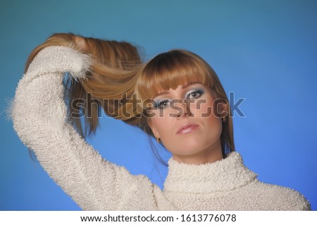 portrait of a beautiful long-haired blonde in a studio on a blue background in a white sweater