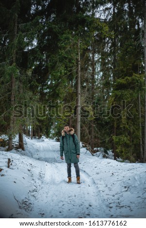 Attractive man standing in winter down jacket, man in warm coat in snow-covered winter forest, jeans, nature, attractive, happy, lifestyle, travel, winter holidays, road, hiking