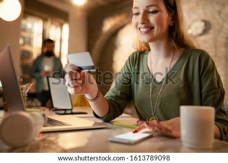 Happy businesswoman using credit card and smart phone for online shopping while working late in the office.