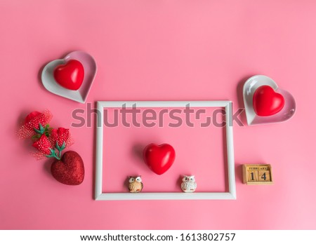 Creative  Valentine  Day  concept  setting  with  white  blank  wooden  picture  frame,  red  hearts  shape,two  simulated  owl  and  rose  on  pink  background