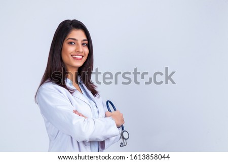 Medical concept of Indian beautiful female doctor in white coat with stethoscope, waist up. Medical student. Woman hospital worker looking at camera and smiling, studio, gray background Royalty-Free Stock Photo #1613858044