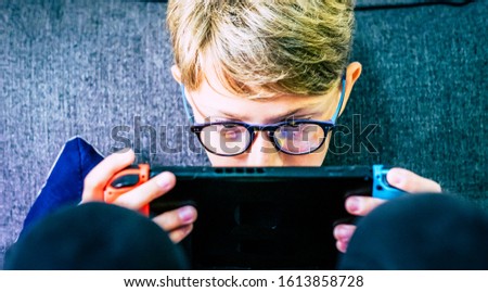 Young and concentrated caucasian child gamer with portable device playing with technology games internet connected with friends - video game addiction to console and obsession Royalty-Free Stock Photo #1613858728