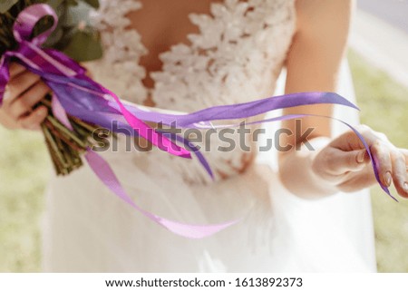 The bride holds a wedding bouquet. Flowers tied with ribbons of purple and violet. The girl touches the ribbons that fly in the wind.