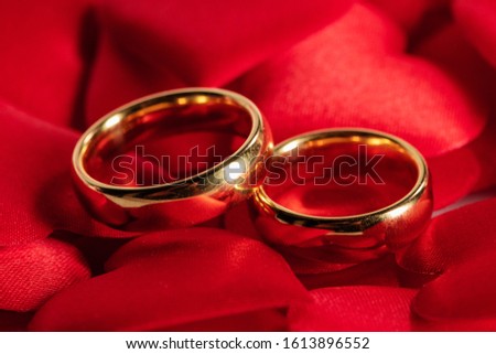 Two golden wedding rings on red satin hearts background
