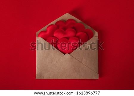Valentine day love letter, envelope of craft paper with red hearts heap spread on red background.