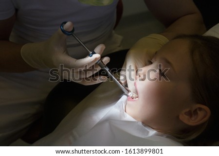 Little girl at dentist office, getting local anesthesia injection into gums, dentist numbing gums for dental work. Pediatric dental care concept. 