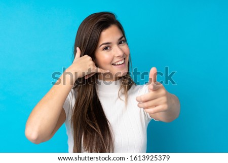 Teenager girl over isolated blue background making phone gesture and pointing front