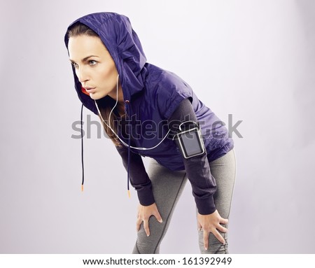Young caucasian woman taking breath after jogging. Female athlete resting with hands on knees and looking away over grey background