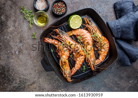 Grilled giant tiger prawns in frying pan with lemon and spices on vintage dark background, top view, copy space. Seafood dinner.