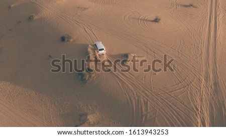Aerial shot of an unknown white SUV driving fast along sand dunes in the desert, UAE