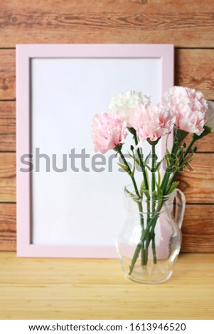 Pastel artificial carnation flower in jug with blank pink picture frame behind on wooden background, Valentine's Day, Mother's Day or Birthday background, Copy space