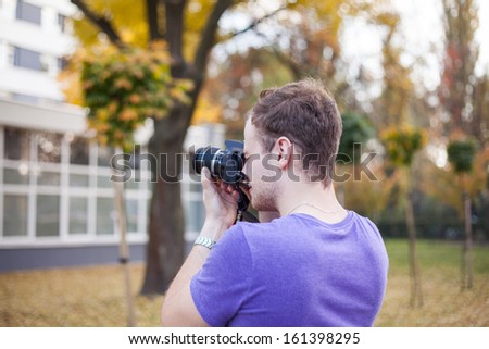 Young man taking outdoor picture with digital camera DSLR.