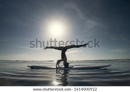 Yoga Headstand Variation Sea Background. A woman performing a headstand with gymnastic longitudinal twine on longboard in the sea