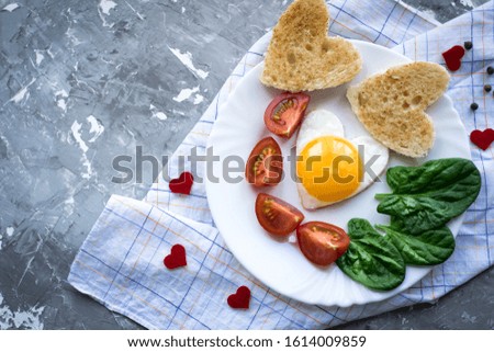 breakfast on Valentine's Day fried eggs and bread in the shape of a heart and fresh vegetables. Text for space. Valentine's background.