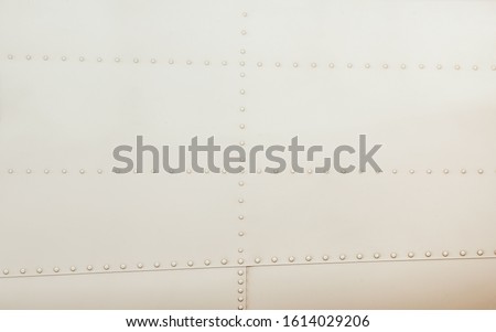 Silver metal surface of the aircraft fuselage with rivets. Fuselage detail view. Airplane metallic fuselage detail with rivets. Royalty-Free Stock Photo #1614029206